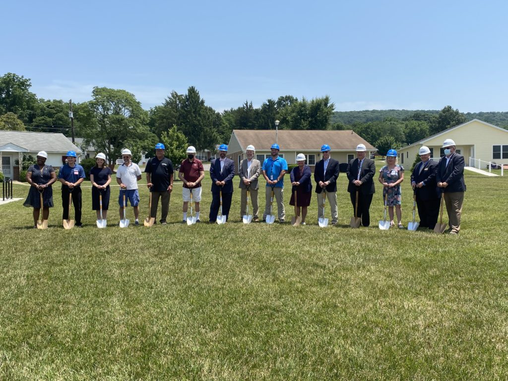 15 individuals men and women holding shovels lined up to break ground in a field of grass